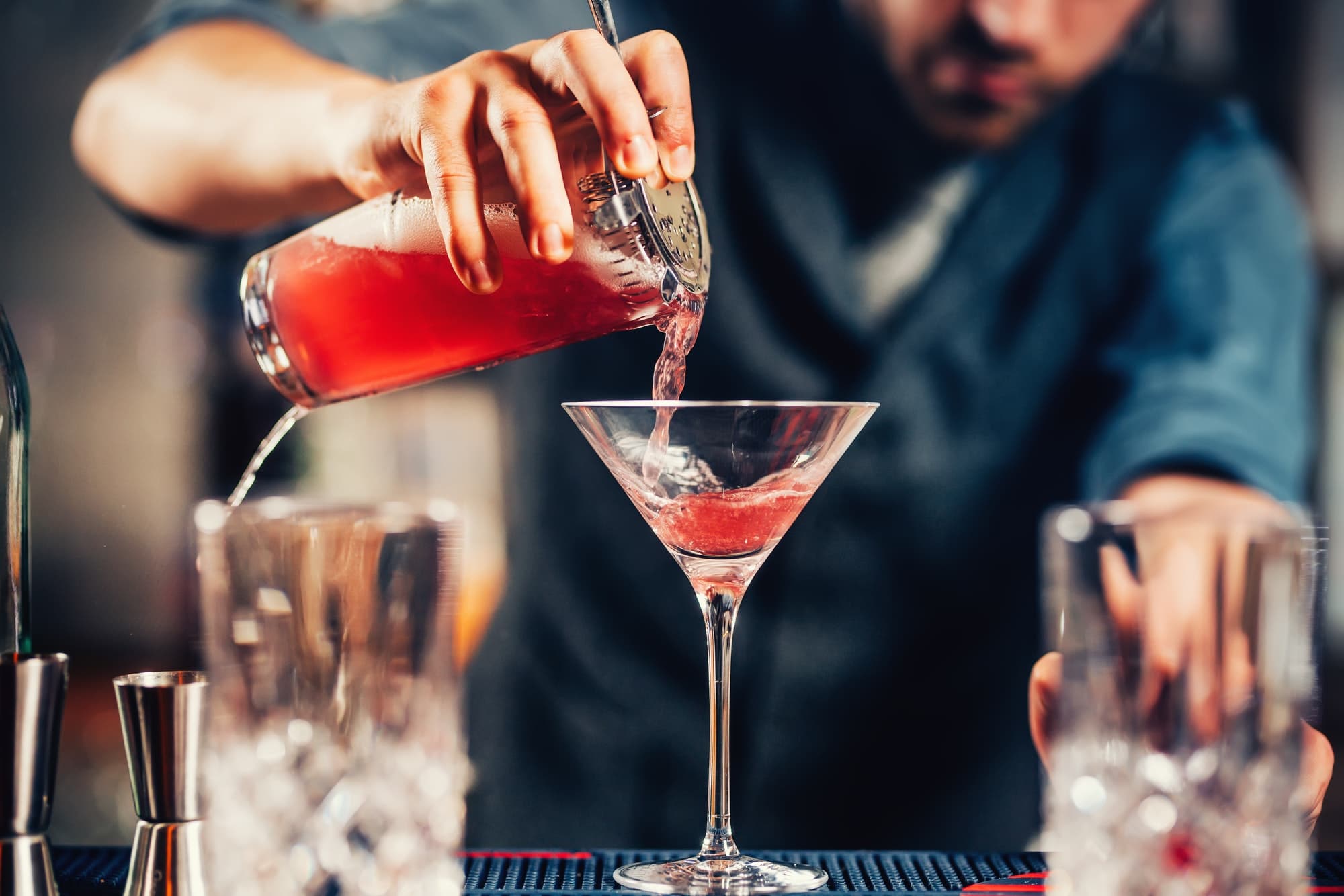 Close up details of barman pouring vodka cosmopolitan cocktail in martini glass